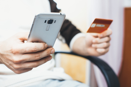 men hands, holding the phone and a credit card or another, entering data from the cardの写真素材