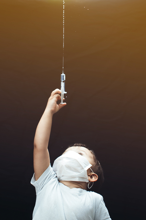 The child in the mask of the doctor with syringe in hands sprinkles, pours on a black backgroundの写真素材