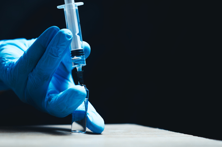 on a black background, the hands in blue gloves gaining medicine into the syringe from the vialの写真素材