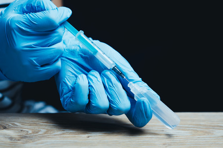 on a black background, the hands in blue gloves gaining medicine into the syringe from the vial