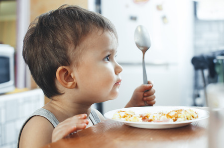 child t-shirt in the kitchen eating scrambled eggs, with a spoonの写真素材