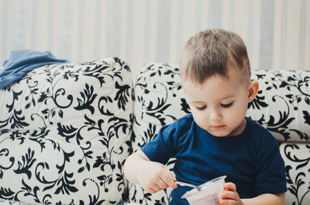 baby boy sitting on the couch in your underwear eating yogurt in the comfort of homeの写真素材