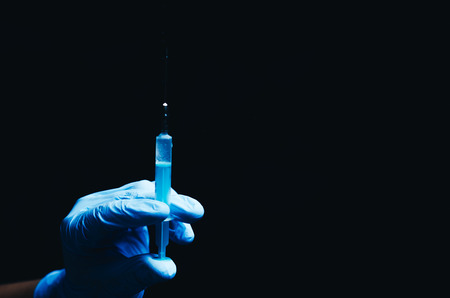 in the hand in a blue glove syringe on black backgroundの写真素材