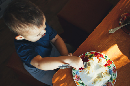 A hungry child is eating dumplings in the kitchen sitting in a chair in a white t-shirtの写真素材
