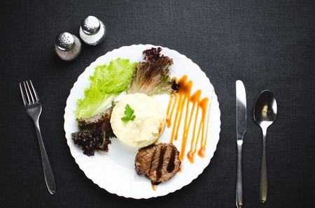 On a white plate, on a beautiful fabric and dark background mashed potatoes with beef meat beautifully polished balsamic sauceの写真素材