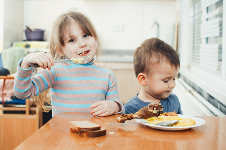 Children in the kitchen eat meat and mashed potatoes, very fun, share and feed each otherの写真素材