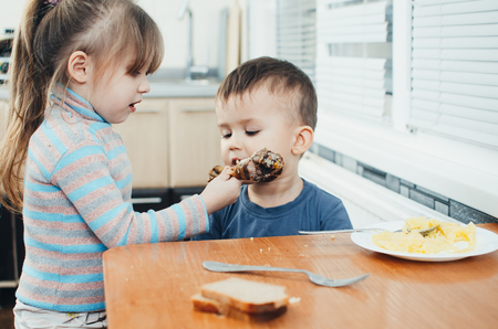 Children in the kitchen eat meat and mashed potatoes, very fun, share and feed each otherの写真素材