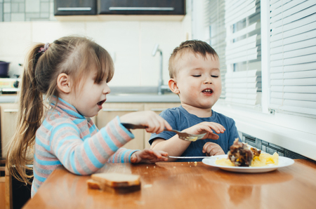 Children in the kitchen eat meat and mashed potatoes, very fun, share and feed each otherの写真素材