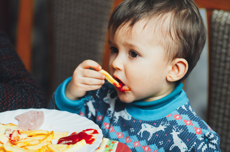 child eating fries with your hands at a birthday party eagerly in a blue sweaterの写真素材