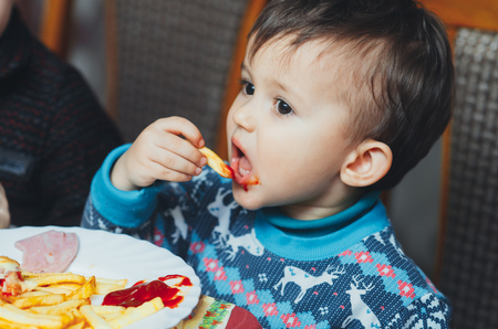 child eating fries with your hands at a birthday party eagerly in a blue sweaterの写真素材