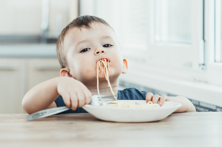 A beautiful cheerful child eats pasta with his hands, spaghetti all dirtyの写真素材