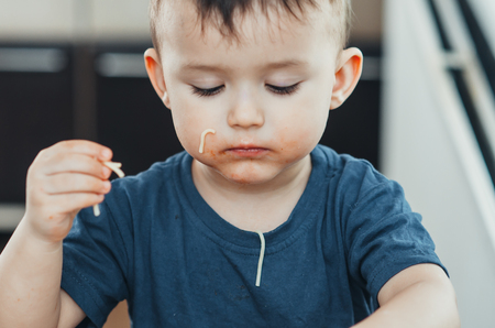 A beautiful cheerful child eats pasta with his hands, spaghetti all dirtyの写真素材