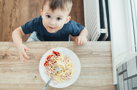 The child in the kitchen at the table eating macaroni and interesting view from the topの写真素材