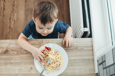 The child in the kitchen at the table eating macaroni and interesting view from the topの写真素材