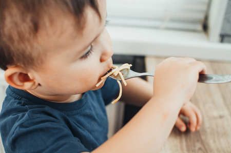 The child in the kitchen at the table eating macaroni and interesting view from the topの写真素材