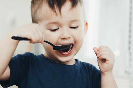 beautiful cute baby eats rice with a spoon in the kitchen, very funの写真素材