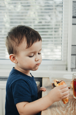 Beautiful baby sitting in the kitchen eating a delicious tube of condensed milkの写真素材