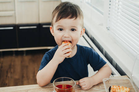 Beautiful baby sitting in the kitchen eating a delicious tube of condensed milkの写真素材