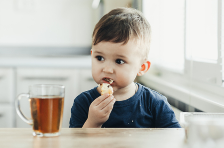 Beautiful baby sitting in the kitchen eating a delicious tube of condensed milkの写真素材