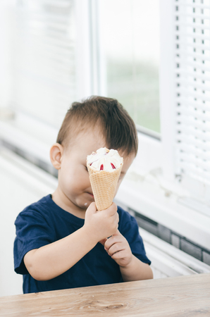A child in a dark-blue t-shirt in the bright kitchen eating a waffle ice cream cone in the summer houseの写真素材