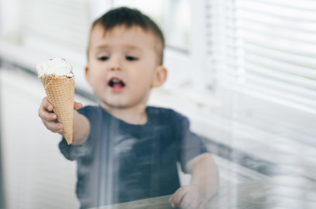A child in a dark-blue t-shirt in the bright kitchen eating a waffle ice cream cone in the summer houseの写真素材