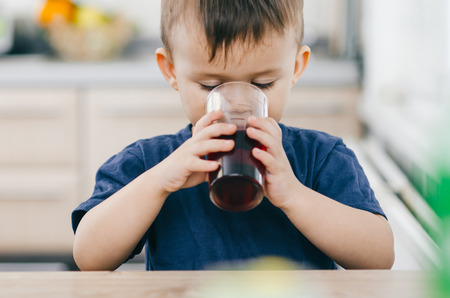 charming baby in the kitchen in the summer drink of pomegranate or cherry juice red colorの写真素材