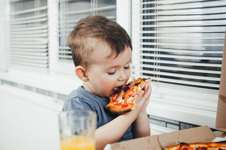 The child in the kitchen eats a huge pizza and drinks juice, a lot of funの写真素材