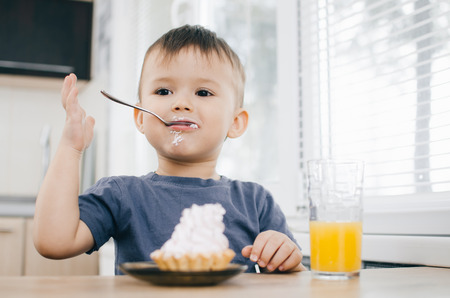 the child in the kitchen eating a cake with cream is very appetizing, spoonの写真素材