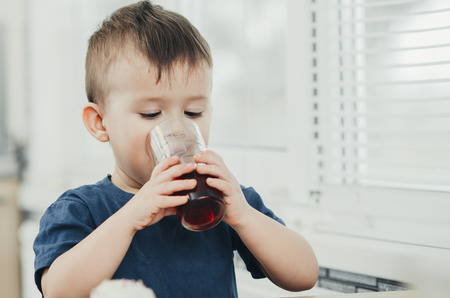 charming baby in the kitchen in the summer drink of pomegranate or cherry juice red colorの写真素材