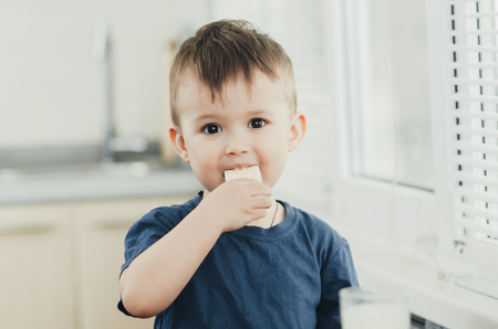 a little charming boy eats waffles in the kitchen and drinks milkの写真素材