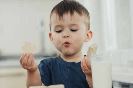a little charming boy eats waffles in the kitchen and drinks milkの写真素材