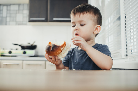 the child in the kitchen eating a sweet bun, very tastyの写真素材