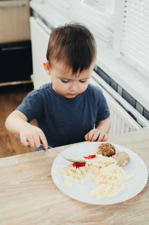 little baby boy in the kitchen eating pasta with cutlets, very tastyの写真素材