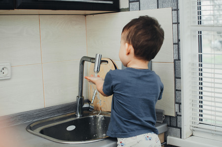The little boy washes his hands under the crane on his ownの写真素材