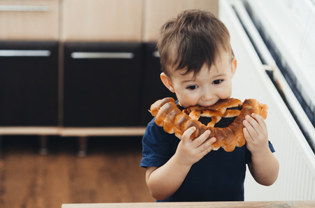 baby in the kitchen eating a big bun or pie with chocolate and condensed milk all dirtyの写真素材