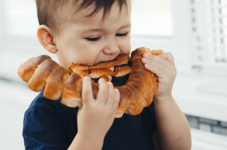 baby in the kitchen eating a big bun or pie with chocolate and condensed milk all dirtyの写真素材