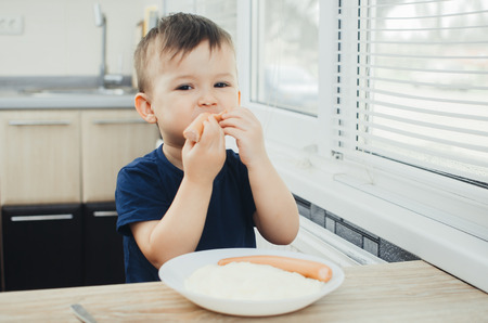 baby eating sausage in the kitchen is very charming and emotionalの写真素材