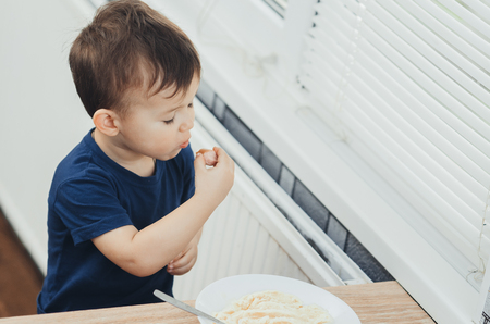 baby eating sausage in the kitchen is very charming and emotionalの写真素材