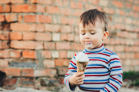 little cute boy   eating ice cream  on brick wall backgroundの写真素材