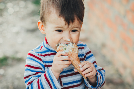 little cute boy   eating ice cream  on brick wall backgroundの写真素材