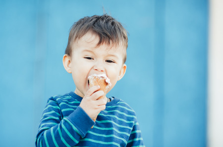 child outdoors, on a blue background eating ice creamの写真素材