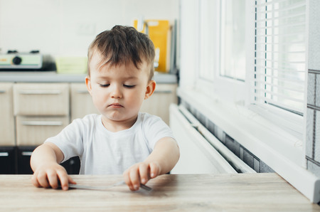 child sits at the table and takes a fork, on the table there is nothingの写真素材