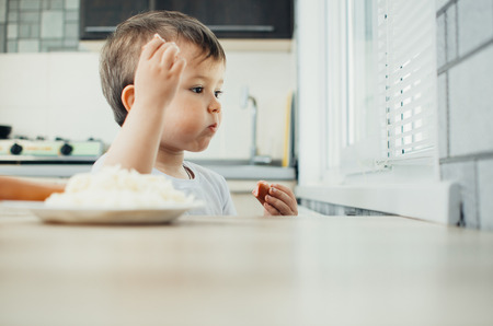 baby in the kitchen eating fun pasta with sausageの写真素材