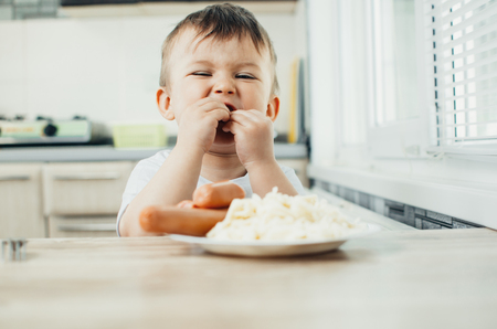 baby in the kitchen eating fun pasta with sausageの写真素材