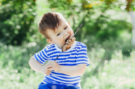 A child eats a kebab on a skewer, in a Park or forest nature green background of trees and grassの写真素材
