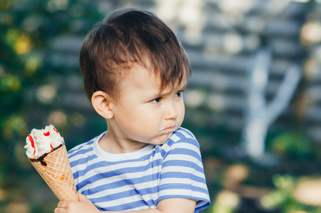 a child in a t-shirt on a bench eating ice cream in the summer, very hot and tastyの写真素材