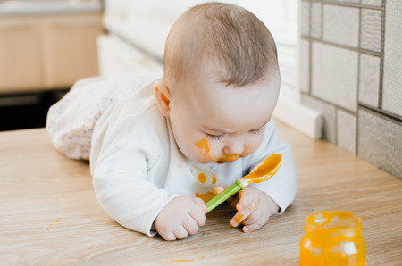 beautiful baby chest all dirty in fruit puree, pumpkin with spoon in hand next to a jar of foodの写真素材