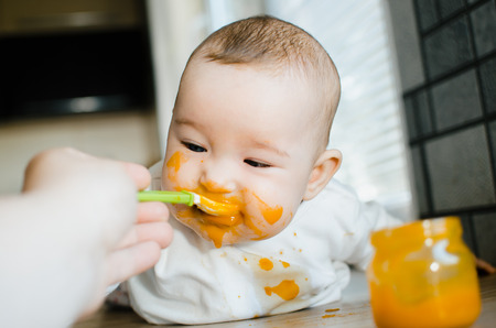 dirty baby in pumpkin puree eats spoonの写真素材