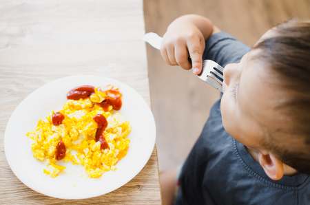A child in a t-shirt in the kitchen eating an omelet, a forkの写真素材