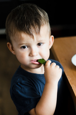 the child in the kitchen eating fresh cucumber and omeletの写真素材